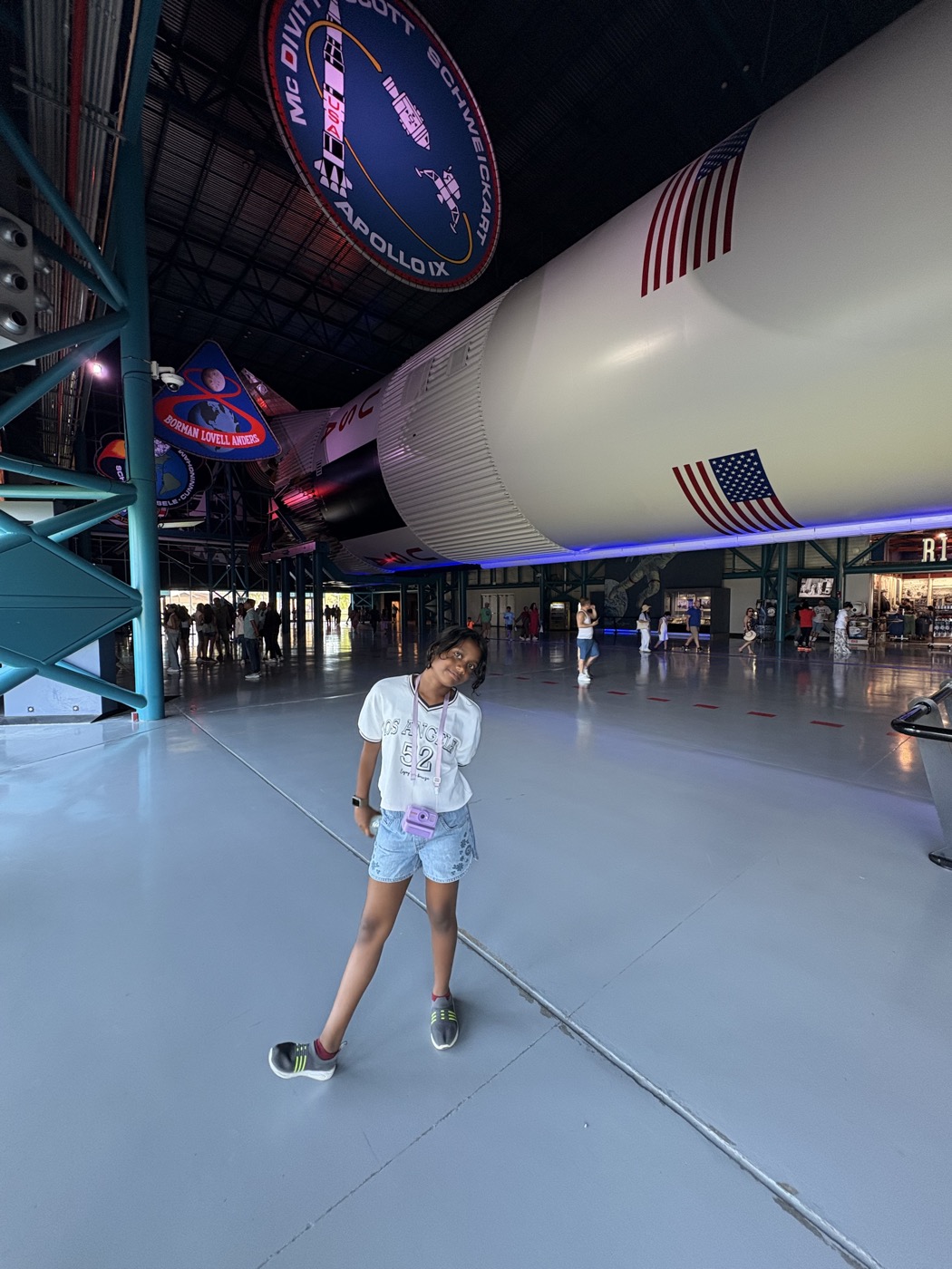 Tanya standing beneath the full Saturn V rocket, Apollo mission patches overhead